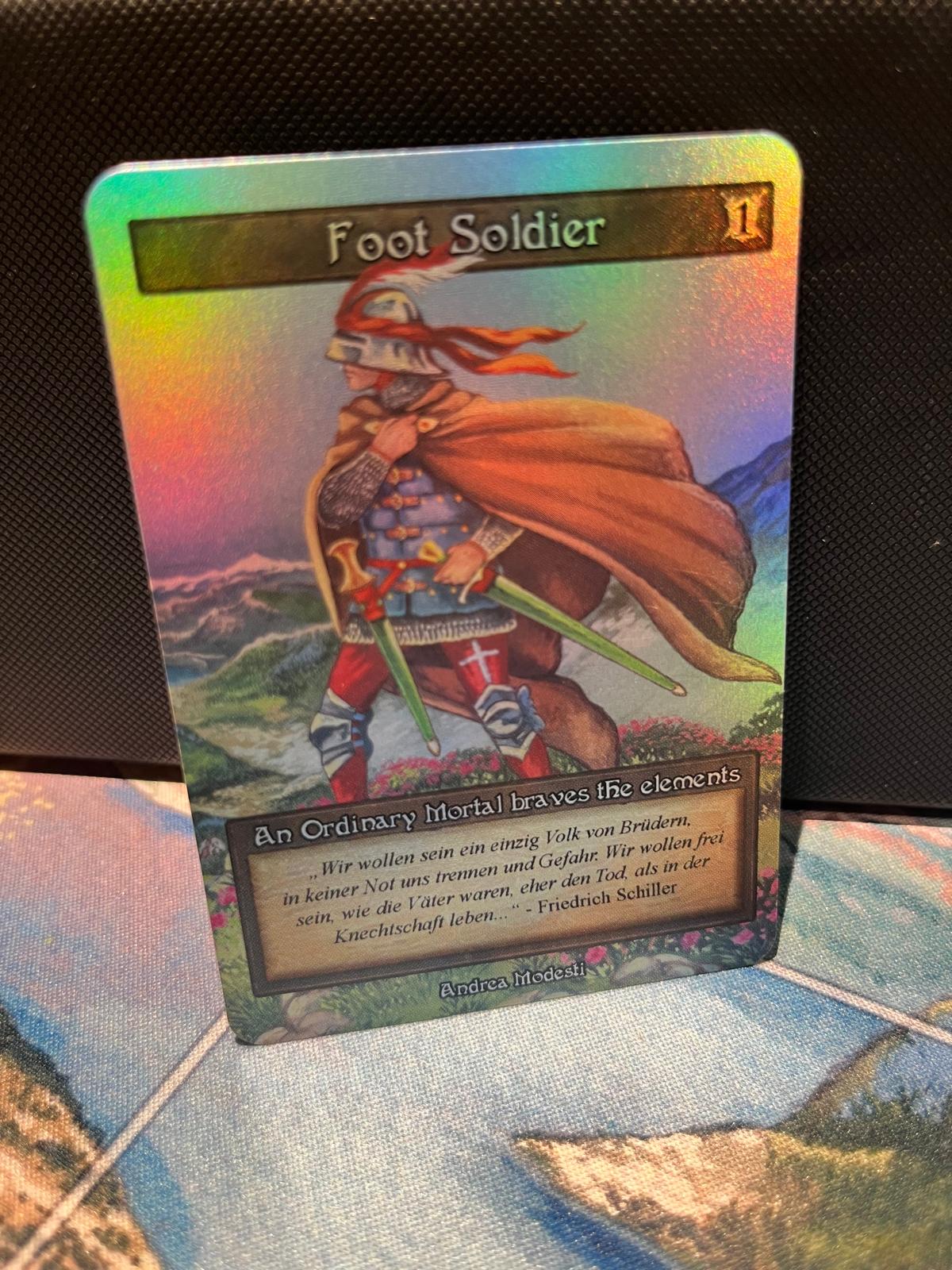 Foot Soldier promo token — photograph of the physical foil “Foot Soldier” trading card, cost 1, art by Andrea Modesti, with a German Schiller quote